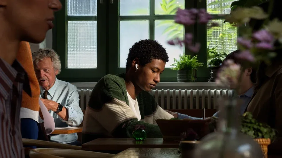 Person wearing AirPods 5 while working in a busy cafe